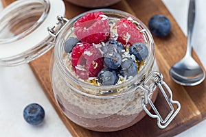 Layered chocolate and peanut butter chia seed pudding in jar, garnished with raspberry, blueberry, honey and coconut flakes,