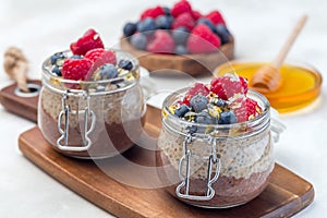 Layered chocolate and peanut butter chia seed pudding in jar, garnished with raspberry, blueberry, honey and coconut flakes,