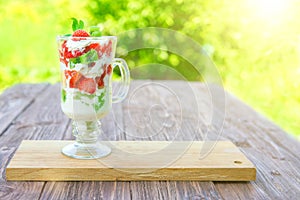 layered dessert with strawberries and cream cheese on wooden table over green garden background