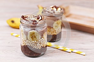 Layered healthy dessert with banana fruit slices, puffed quinoa grain and chocolate chia seed pudding in jar