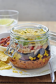 Layered Mexican sandwich jar with black beans, lettuce, cheese, red peppers, lettuce and tortilla chips