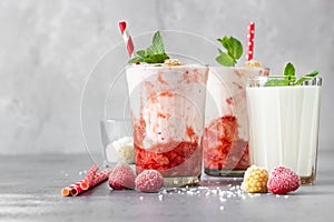 Layered strawberry and raspberry smoothie or milkshake in glasses decorated with mint, raspberry and coconut flakes on grey table