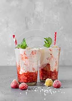 Layered strawberry and raspberry smoothie or milkshake in glasses decorated with mint, raspberry and coconut flakes on grey table