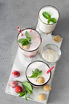 Layered strawberry and raspberry smoothie or milkshake in glasses decorated with mint, raspberry and coconut flakes on grey table