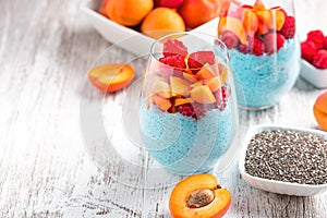 Layered superfoods pudding with apricot, raspberry, chia in glasses on white wooden background. Mousse with chia seeds, berries