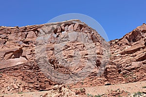 Layers of Entrada Sandstone behind the road leading into Arches National Park contrasted against a clear, blue sky