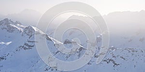 Layers of mountain peaks covered with snow, in Winter, with light shining through fog and mist - view from Terrazza Delle Dolomiti