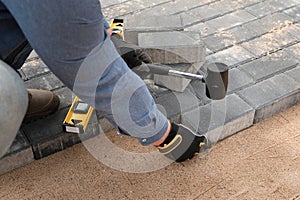 Laying cement pavement on a walkway with a rubber hammer and gloves on a sand. House improvement