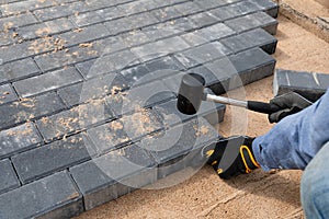 Laying cement pavement on a walkway with a rubber hammer and gloves on a sand. House improvement