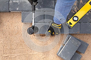 Laying cement pavement on a walkway with a rubber hammer and gloves on a sand. House improvement