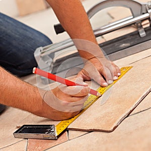 Laying ceramic floor tiles - man hands marking tile to be cut, c