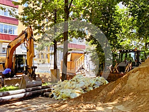 Laying communications in the yard. excavator digs holes for laying plumbing pipes. nearby are building materials in sealed bags
