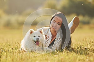 Laying down on the ground. Woman with her dog is having fun on the field at sunny daytime