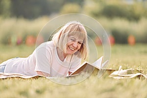 Laying down and reading book. Senior woman having nice weekend outdoors on the field at sunny day