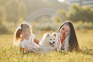 Laying down together. Woman and little girl have a walk with dog on the field at sunny daytime