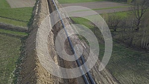 Laying gas pipeline among green hills. Large high-pressure steel pipes prepared for immersion in the excavated trench. Land works