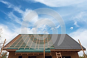 Laying metal tile on the roof. House under construction with screwdriver and roofing iron.