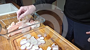 Laying onions cut into rounds on the sliced chicken. On a kitchen wooden cutting board, slice peeled onions. Preparing