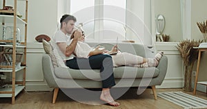 Laying on the sofa a young couple watching something from laptop and eating popcorn , cozy atmosphere around. shot on