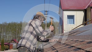 Laying of soft tiles. Bitumen roofing. Hammering nails with a hammer.