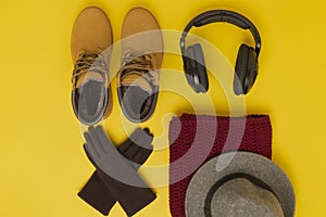 Layout of autumn clothes and accessories in warm colors on a yellow background. Gloves, headphones boots, hat and scarf flat lay