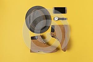 Layout of autumn clothes and accessories in warm colors on a yellow background. Hat, boots, phone and watch flat lay nearby