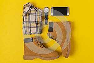 Layout of autumn clothes and accessories in warm colors on a yellow background. Jeans, shirt, boots, phone and watch flat lay