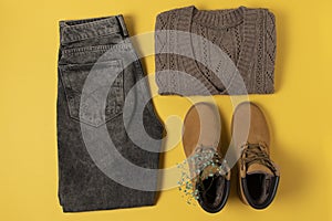Layout of autumn clothes in warm colors on a yellow background. flat lay nearby Jeans, jumper, boots