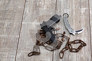 The layout of a black pistol, several scattered cartridges, a folding knife and an old rusty chain.