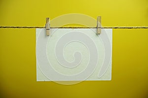 Layout of Empty paper card space for text hanging on the wall with Clothespins on string against yellow background