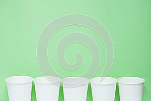 The layout on a green background from white paper disposable cups. Caring for the environment. Recycling garbage