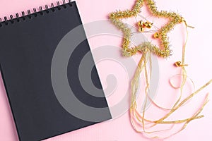 Layout for holiday to-do list. black notebook and star of tinsel on pink background. flat lay, copy space, minimal concept