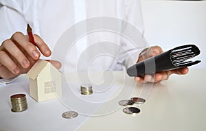 Layout of a house made of white paper and a woman& x27;s hand, a calculator on a white table. The concept of a mortgage.