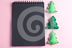 Layout for Merry Christmas to-do list. black notebook on pink background. toys made of felt in the form of green fir trees