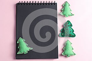 Layout for Merry Christmas to-do list. black notebook on pink background. toys made of felt in the form of green fir trees, top