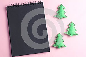 Layout for Merry Christmas to-do list. black notebook and toys made by hand from felt on a pink background. flat lay, copy space,