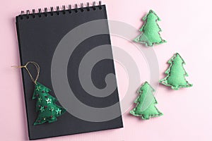 Layout for Merry Christmas to-do list. black notebook and toys made by hand from felt on a pink background. flat lay, copy space
