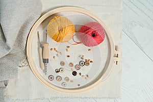 Layout of stretching frame, two balls of yarn, wooden buttons, punch needles and piece of linnen fabric on white wooden floor.