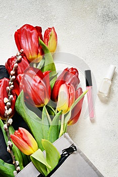 Layout of tulips, backpack and women`s personal belongings on a light-colored concrete background.Flowers, bag, nail polish