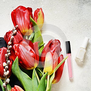 Layout of tulips, backpack and women`s personal belongings on a light-colored concrete background.Flowers, bag, nail polish