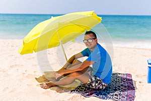 Lazing man in sun under solar umbrella on towel enjoy the lazy time on the beach