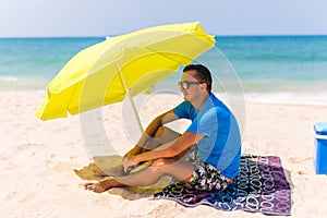 Lazing man in sun under solar umbrella on towel enjoy the lazy time on the beach