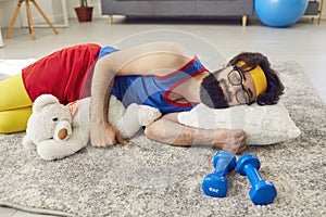 Lazy athlete sleeping peacefully on the floor, hugging a teddy bear, with dumbbells beside