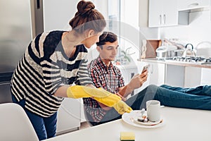 Lazy boyfriend hanging in phone while his girlfriend cleaning his dishes after dinner in kitchen. Family arguement photo