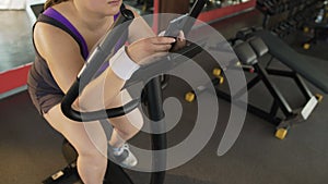 Lazy corpulent female pedaling slowly stationary bike and scrolling on phone