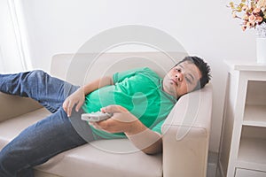 Lazy Fat obese man laying on the couch and watching tv