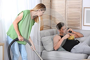 Lazy husband lying on sofa and his wife cleaning