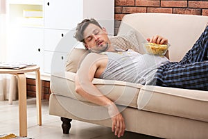 Lazy man with bowl of chips sleeping on sofa