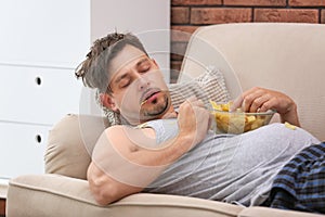 Lazy man with bowl of chips sleeping on sofa photo
