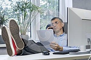 Lazy man feet up on desk examines papers and talking on the phone. Young director working with his feet on the table